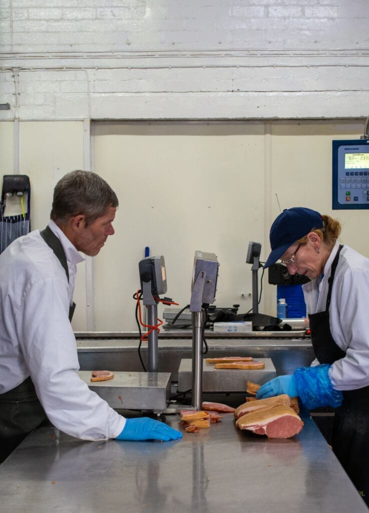 Two workers weighing the slices of bacon