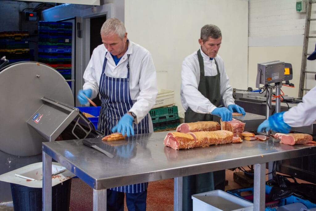Two workers one working the cutting machine, the other weighing the slices